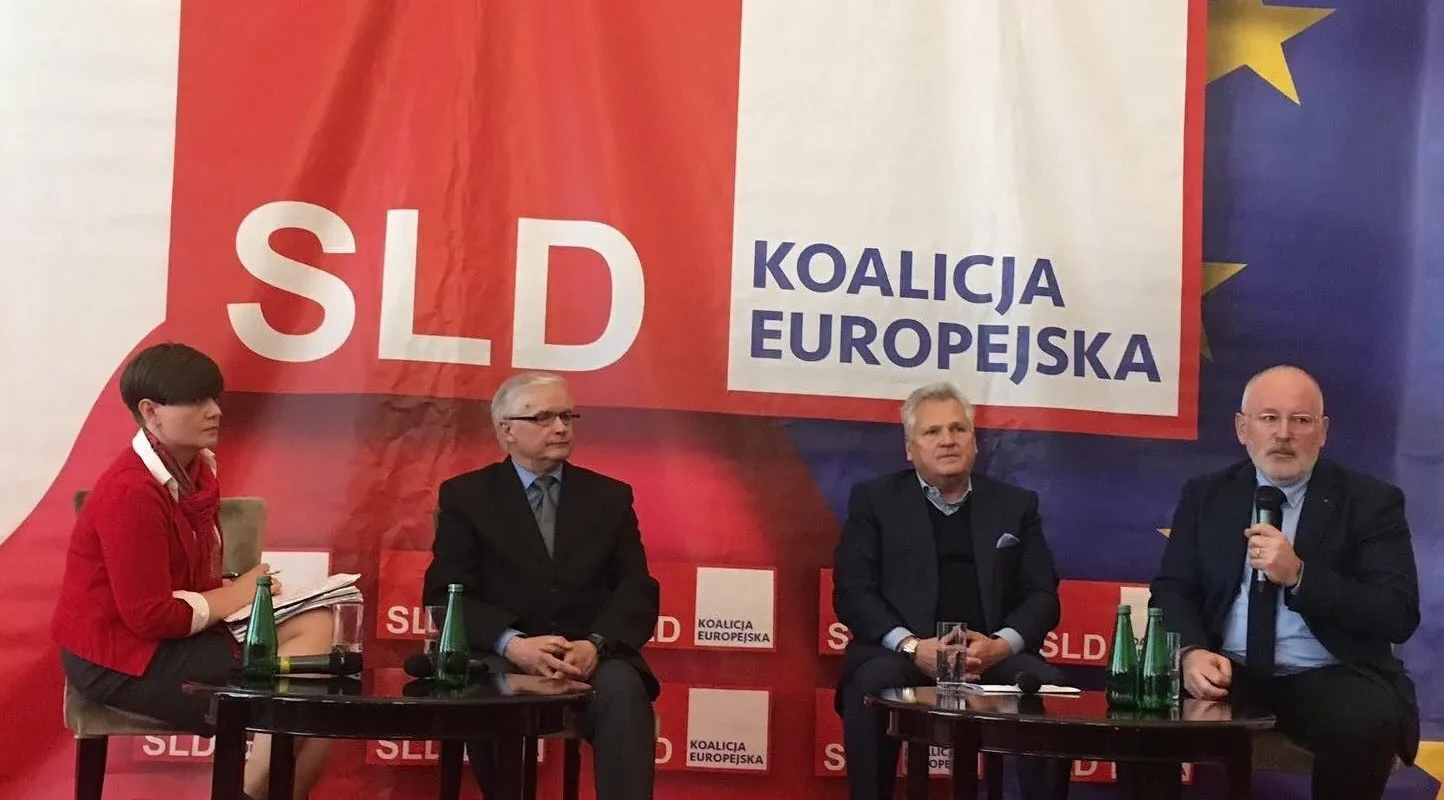 Cztery osoby siedzą na panelu przed dużym banerem SLD Koalicja Europejska i flagą Unii Europejskiej, podczas debaty o Unii Europejskiej.