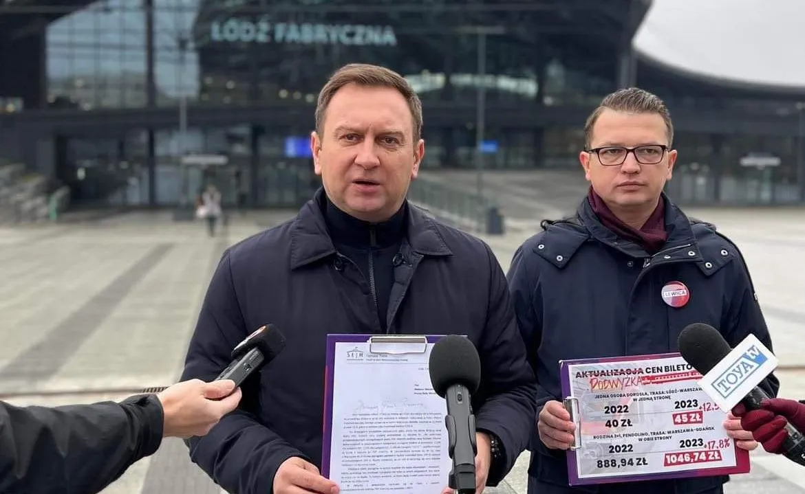 Na zdjęciu widać dwóch mężczyzn w formalnych ubraniach, stojących przed budynkiem stacji Łódź Fabryczna, trzymających dokumenty oraz kartki z informacjami o aktualizacji cen biletów.