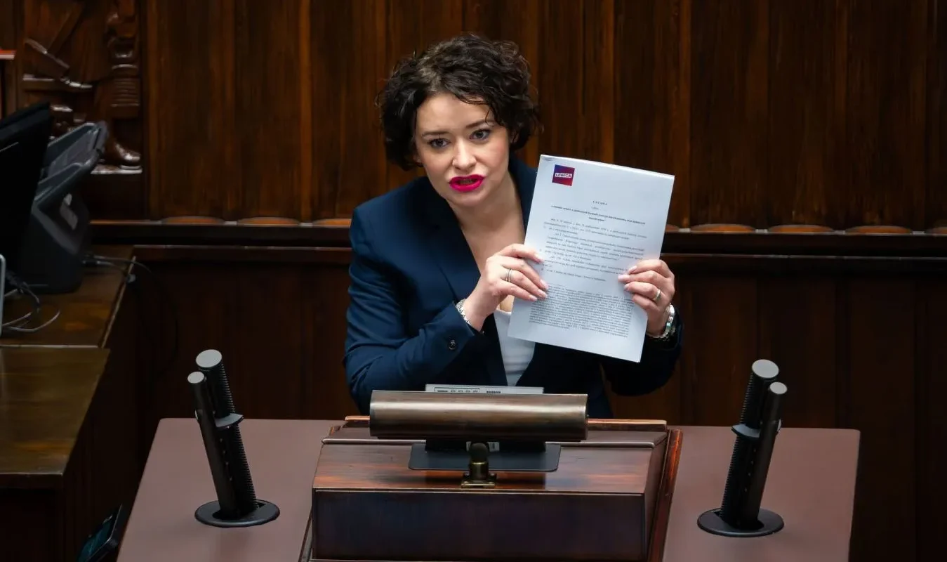 Polityczka Lewicy stoi przy mównicy w parlamencie, prezentując dokument ustawy o budownictwie społecznym podczas wystąpienia.
