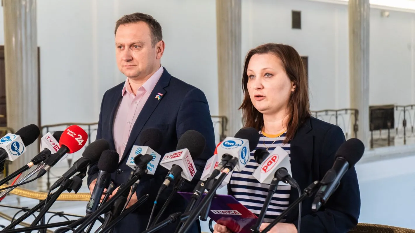 Dwóch przedstawicieli przemawia na konferencji prasowej przed Elektrownią Ostrołęka, otoczonych mikrofonami dziennikarzy.