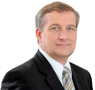 Portret mężczyzny w garniturze na białym tle, z krótkimi szaro-brązowymi włosami i neutralnym wyrazem twarzy.