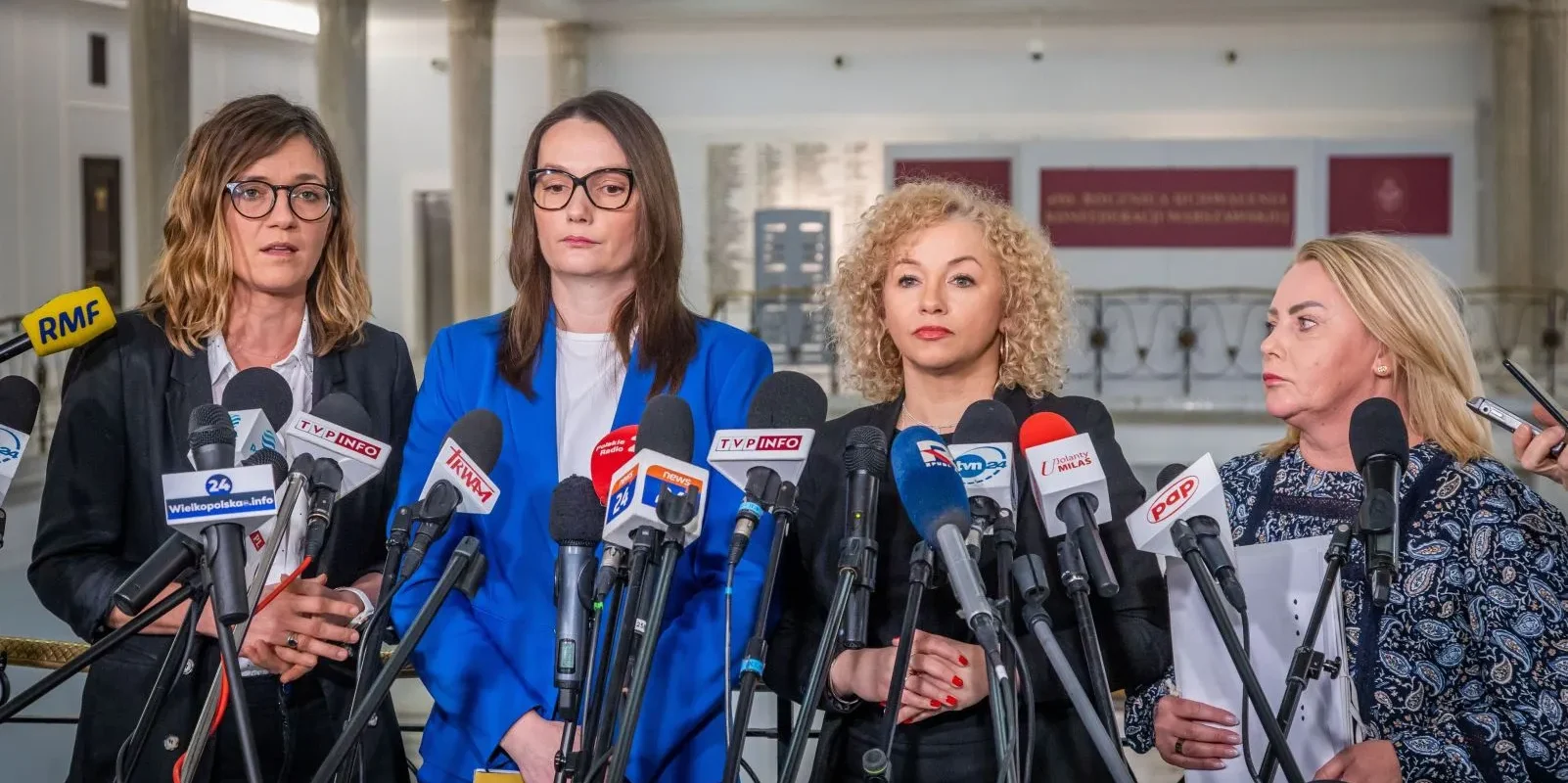 Cztery kobiety w formalnych ubraniach stoją przed zestawem mikrofonów z logotypami polskich mediów podczas konferencji prasowej.