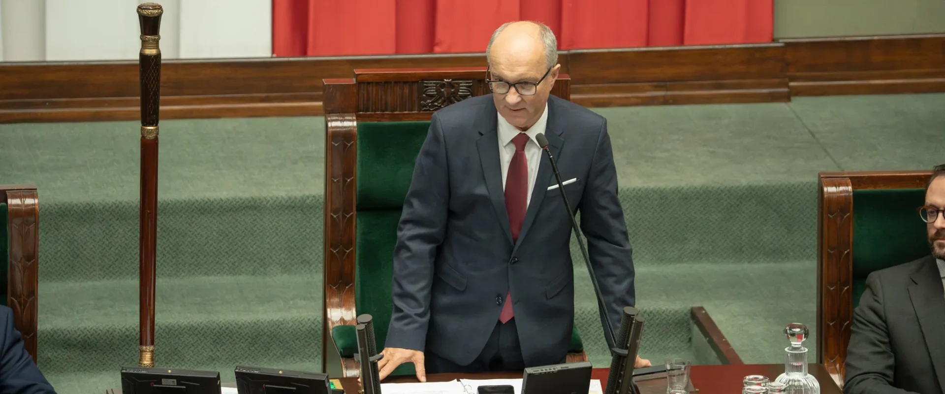 Mężczyzna w garniturze stoi za biurkiem w sali plenarnej Sejmu i przemawia podczas inauguracyjnego posiedzenia jako nowy marszałek Sejmu.