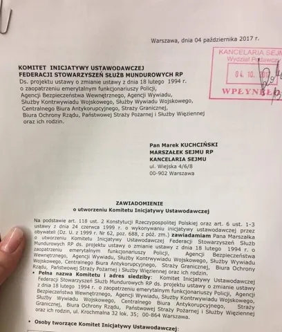 Zdjęcie przedstawia zbliżenie na ostemplowane zawiadomienie Komitetu Inicjatywy Ustawodawczej Federacji Stowarzyszeń Służb Mundurowych RP, adresowane do Marszałka Sejmu i dotyczące projektu ustawy o przywróceniu emerytur mundurowych, trzymane jedną dłonią.