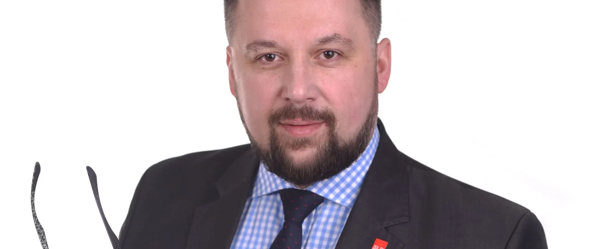 Portret mężczyzny w garniturze na białym tle, trzymającego okulary w dłoni.