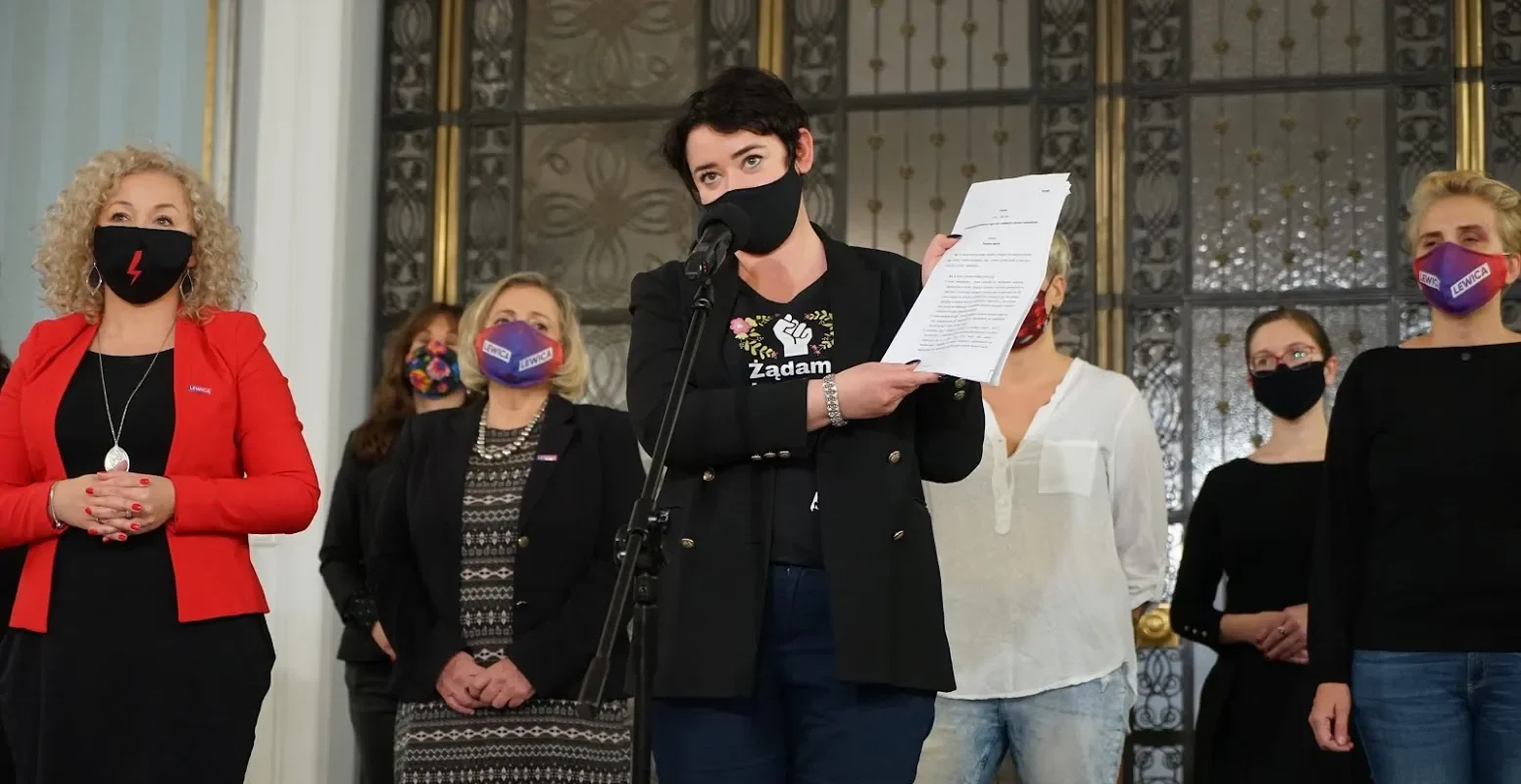 Polityczka przemawia na konferencji prasowej, trzymając dokumenty, otoczona współpracownikami w maseczkach podczas zapowiedzi obywatelskiego projektu ustawy liberalizującego prawo do przerwania ciąży.