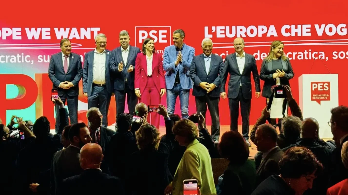 Grupa polityków stoi na scenie podczas wiecu europejskiej socjaldemokracji na czerwonym tle z logiem PSE.