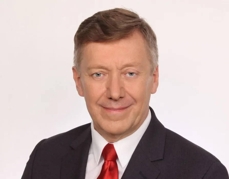 Portret mężczyzny w czarnym garniturze i czerwonym krawacie na jasnym tle.