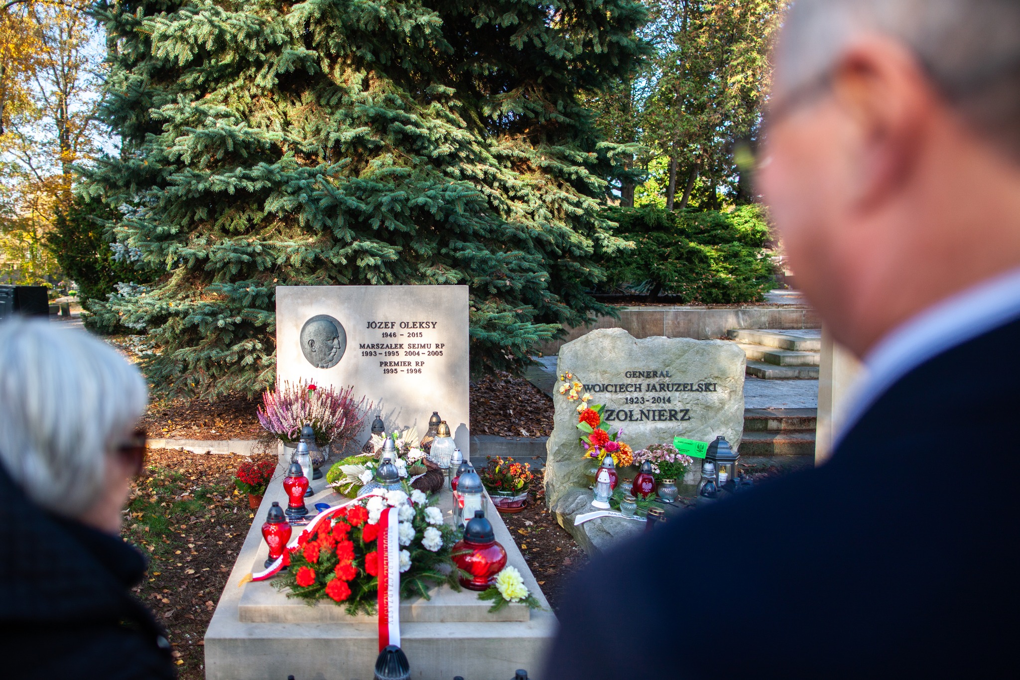Na zdjęciu widoczny jest cmentarz, na którym znajdują się groby Józefa Oleksego i Wojciecha Jaruzelskiego, ozdobione zniczami i kwiatami.