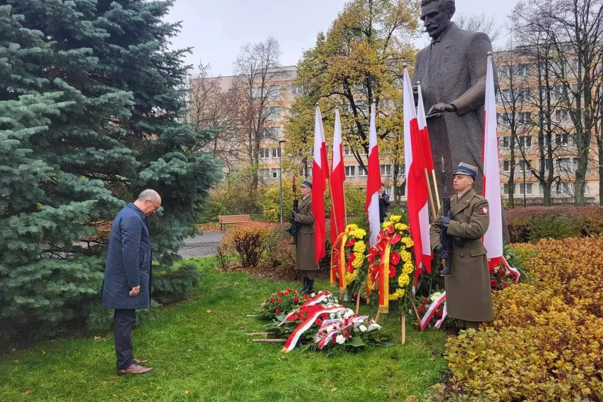Mężczyzna składa hołd przed pomnikiem podczas obchodów Narodowego Święta Niepodległości, wokół stoją polskie flagi, kwiaty i żołnierze w mundurach.