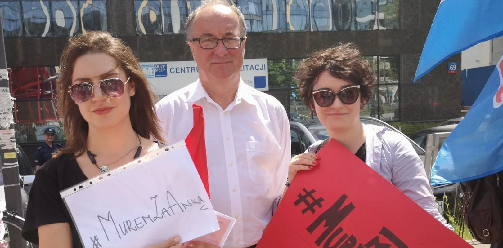 Trzy osoby stoją na ulicy, uśmiechają się i trzymają plakaty wyrażające poparcie dla prawa do zrzeszania się i zakładania związków zawodowych.