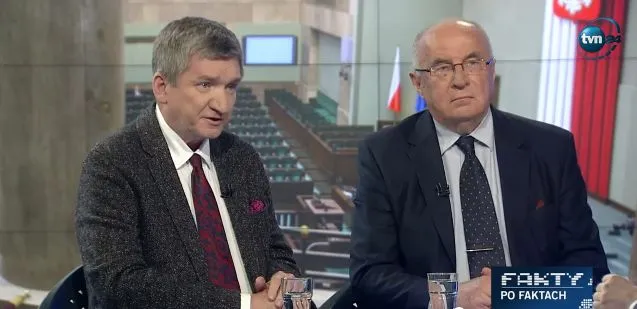 Dwóch mężczyzn w garniturach siedzi w studiu telewizyjnym podczas rozmowy, na tle widać polską flagę.