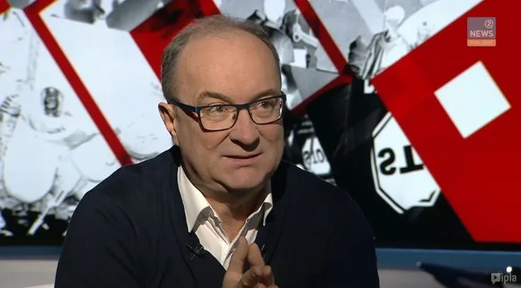 Mężczyzna w okularach siedzi w studiu telewizyjnym i gestykuluje podczas wywiadu na tle czerwono‑białej grafiki, dyskutując o liberalizacji prawa do aborcji.