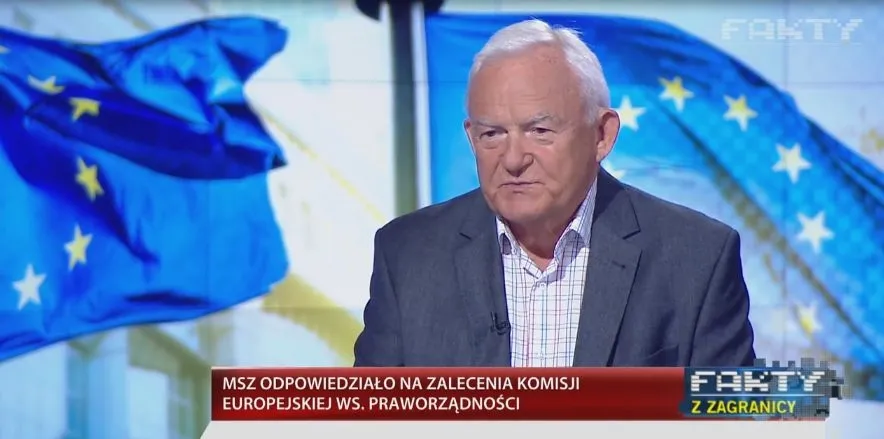 Starszy mężczyzna w marynarce udziela wywiadu w programie telewizyjnym, na tle flag Unii Europejskiej i paska informacyjnego o odpowiedzi rządu na zalecenia Komisji Europejskiej.