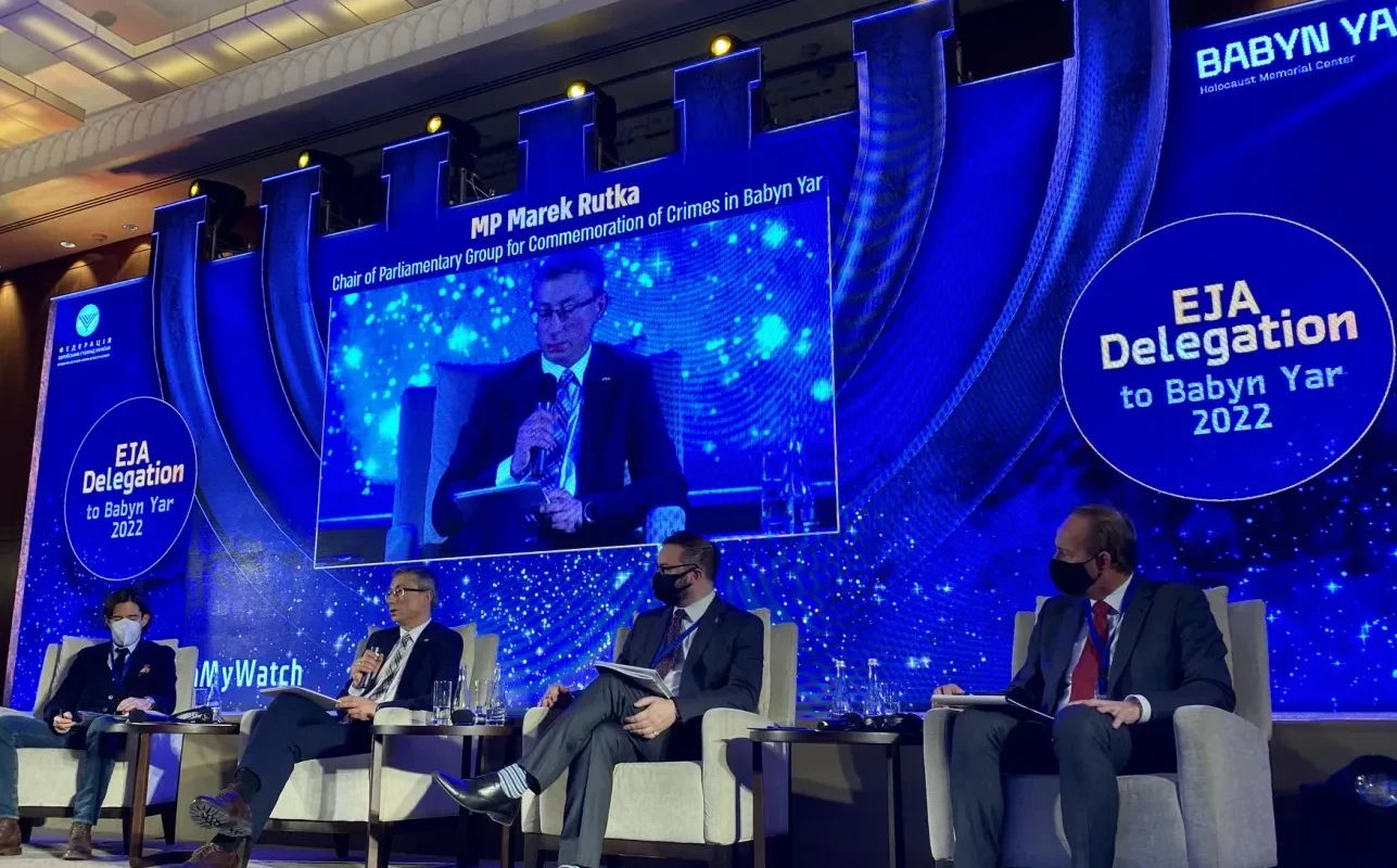 Na zdjęciu przedstawiono panel dyskusyjny z udziałem polityków w trakcie wydarzenia poświęconego upamiętnieniu zbrodni w Babim Jarze, z wyświetlonym w tle wystąpieniem posła Marka Rutki.