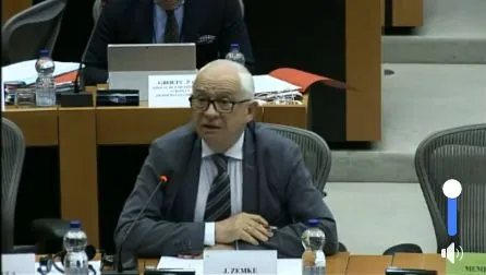 Mężczyzna w garniturze i okularach siedzi przy stole i przemawia do mikrofonu podczas publicznego wysłuchania o prawach żołnierzy w państwach Unii Europejskiej.