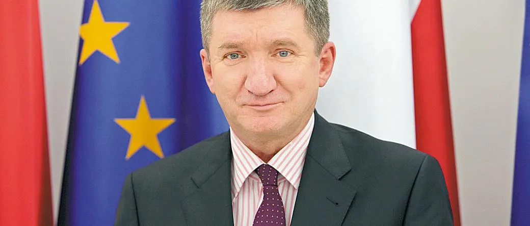 Mężczyzna w garniturze stoi na tle flag Unii Europejskiej i flag państwowych.
