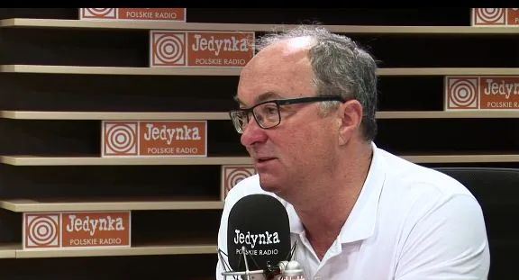 Mężczyzna w okularach siedzi przy mikrofonie w studiu radiowym Jedynka (Polskie Radio).