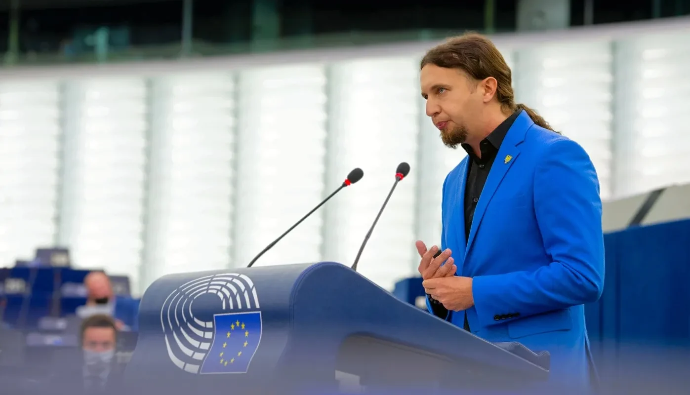 Mężczyzna w niebieskim garniturze przemawia z mównicy w sali obrad Parlamentu Europejskiego.