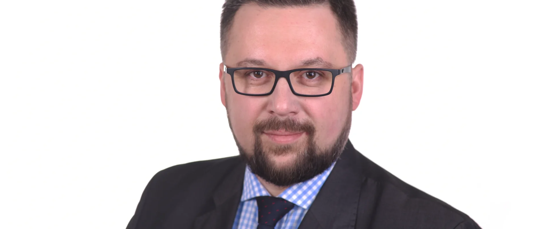 Portret mężczyzny w garniturze i okularach na białym tle, z czerwonym pinem SLD na klapie.