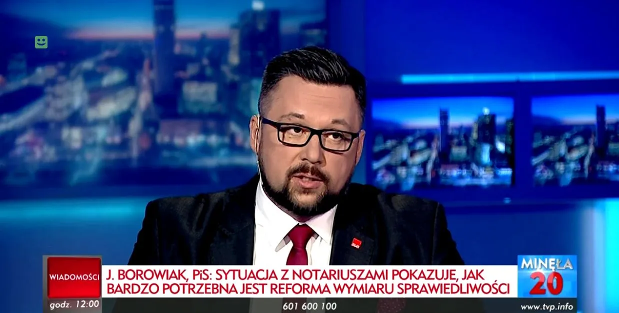 Mężczyzna w czarnym garniturze, białej koszuli, czerwonym krawacie i okularach przemawia w studiu telewizyjnym, a na dole ekranu wyświetlany jest komentarz dotyczący reformy wymiaru sprawiedliwości.