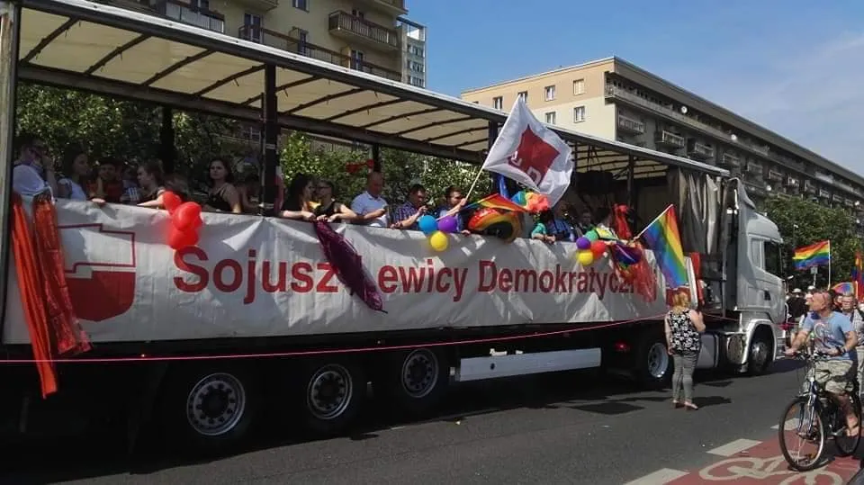 Parada Równości 2019: ciężarówka z banerem Sojusz Lewicy Demokratycznej, udekorowana tęczowymi flagami i balonami, z uczestnikami na pokładzie.