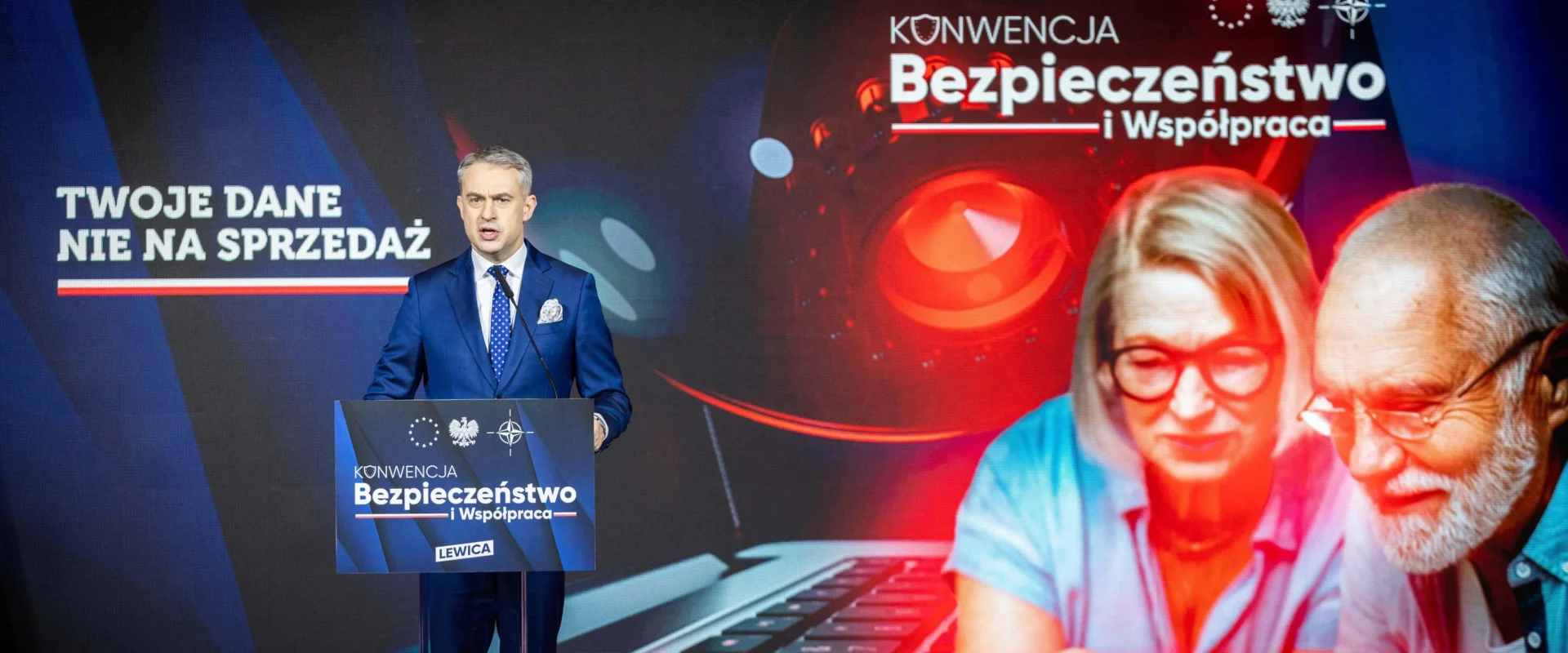 Mężczyzna w granatowym garniturze przemawia z podium podczas konferencji o bezpieczeństwie i współpracy, a w tle widoczna jest grafika z napisem „Twoje dane nie na sprzedaż” oraz para starszych ludzi z laptopem.