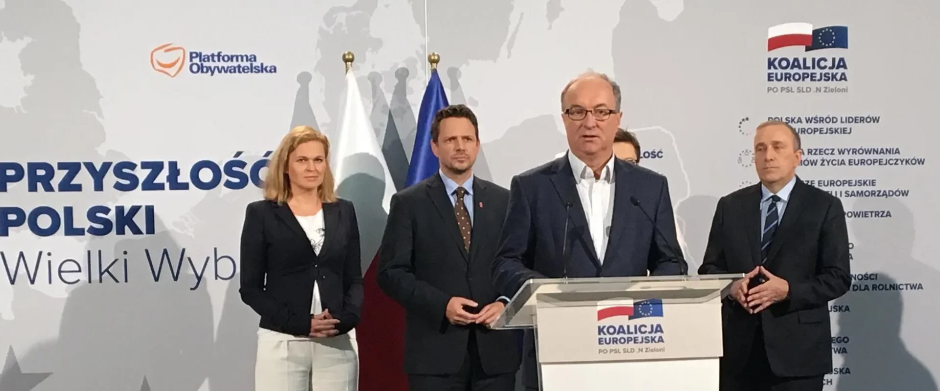 Grupa czterech polityków stojących na konferencji prasowej Koalicji Europejskiej przy mównicy z logo KO, w tle baner z napisem „Przyszłość Polski” oraz flagi.