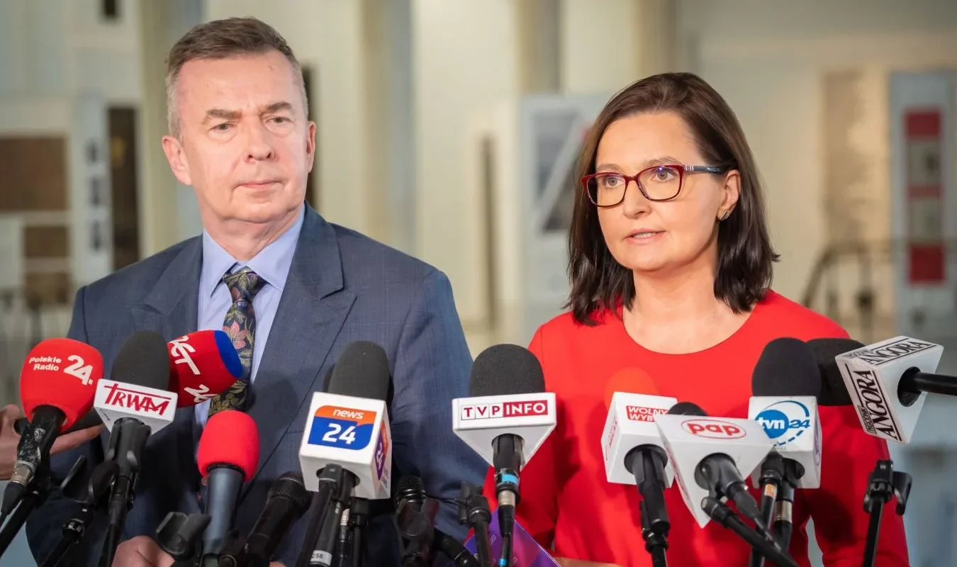 Na zdjęciu widoczni są dwaj mówcy podczas konferencji prasowej, przed którymi ustawione są mikrofony z logo różnych mediów.