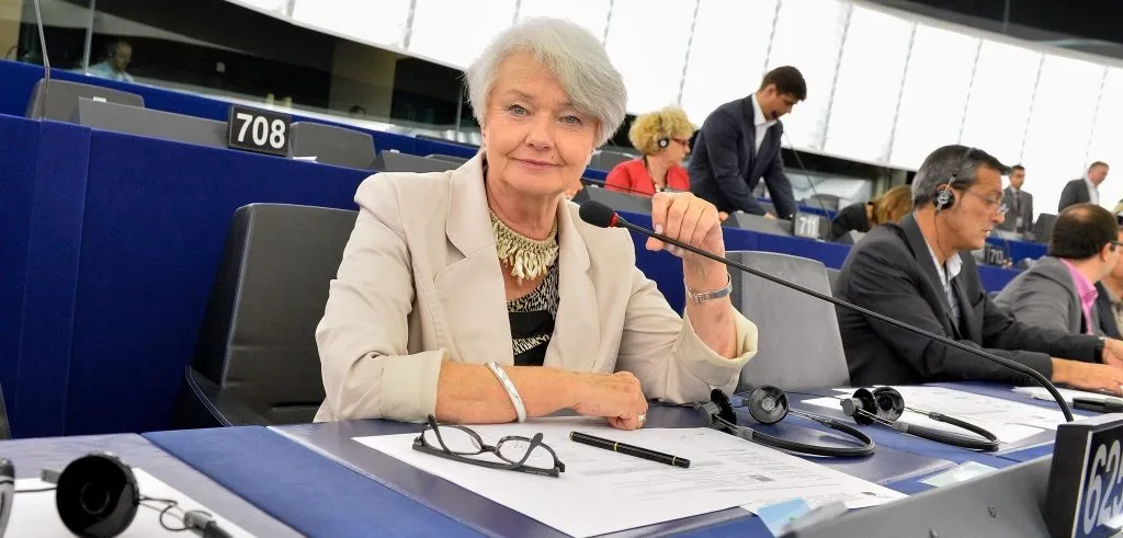 Kobieta siedzi przy stanowisku w sali plenarnej Parlamentu Europejskiego, trzyma mikrofon i spogląda w obiektyw.