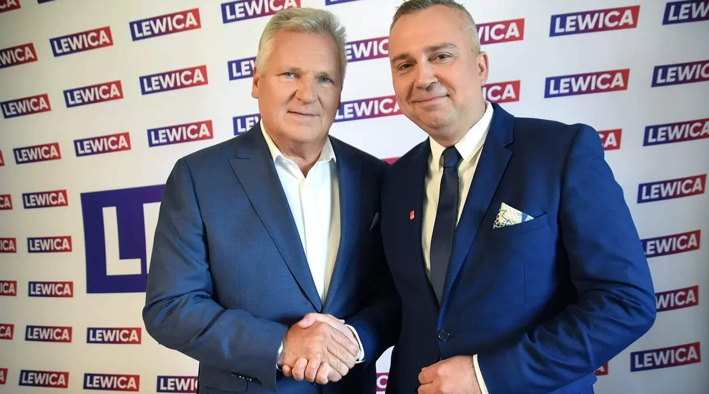 Dwóch mężczyzn w garniturach ściska sobie dłonie na tle baneru z logotypami Lewica.