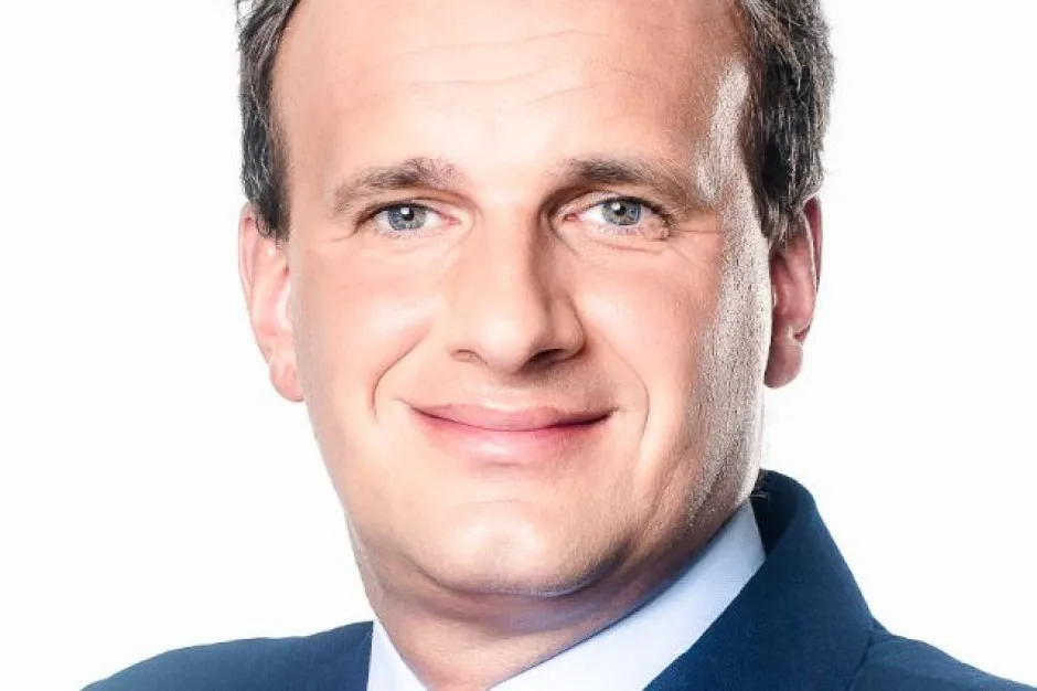 Portret uśmiechniętego mężczyzny w granatowym garniturze na białym tle.