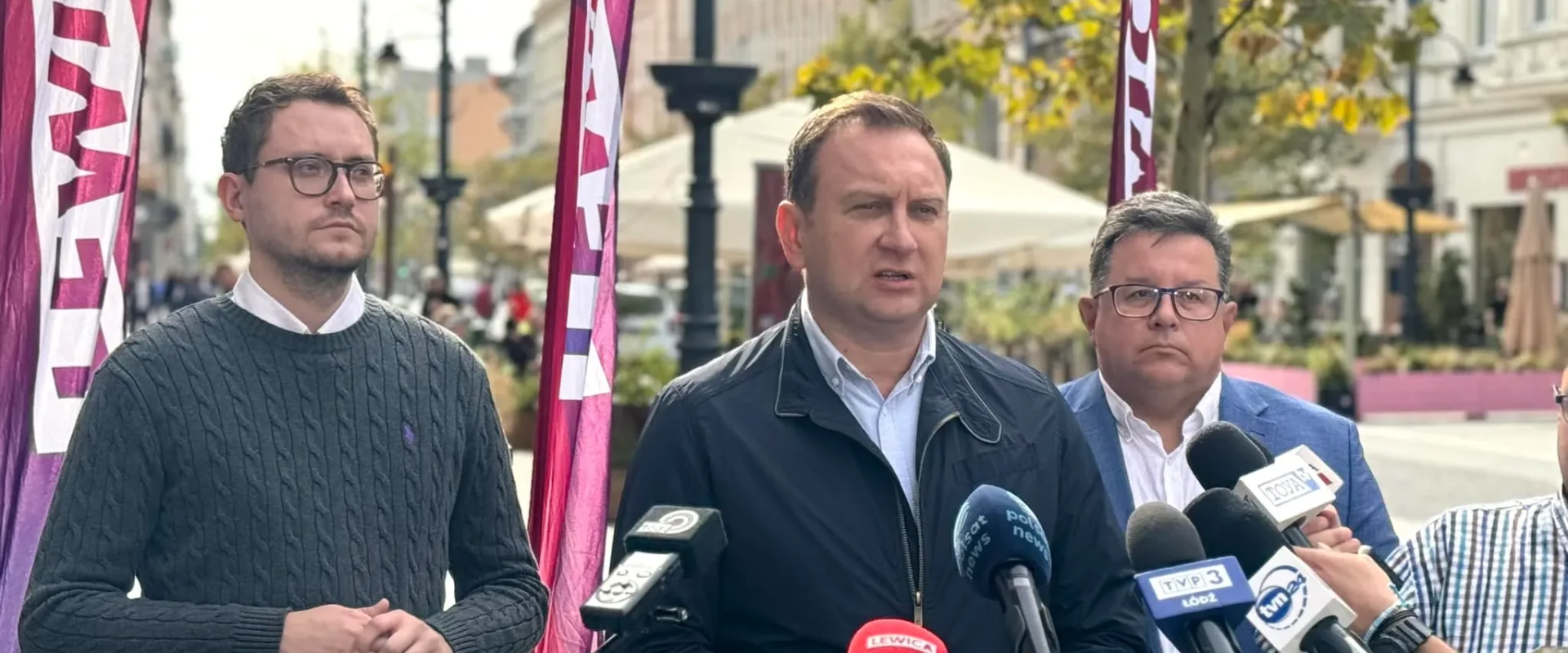 Politycy Lewicy podczas konferencji prasowej na ulicy, stoją przed mikrofonami i flagami partii w tle.