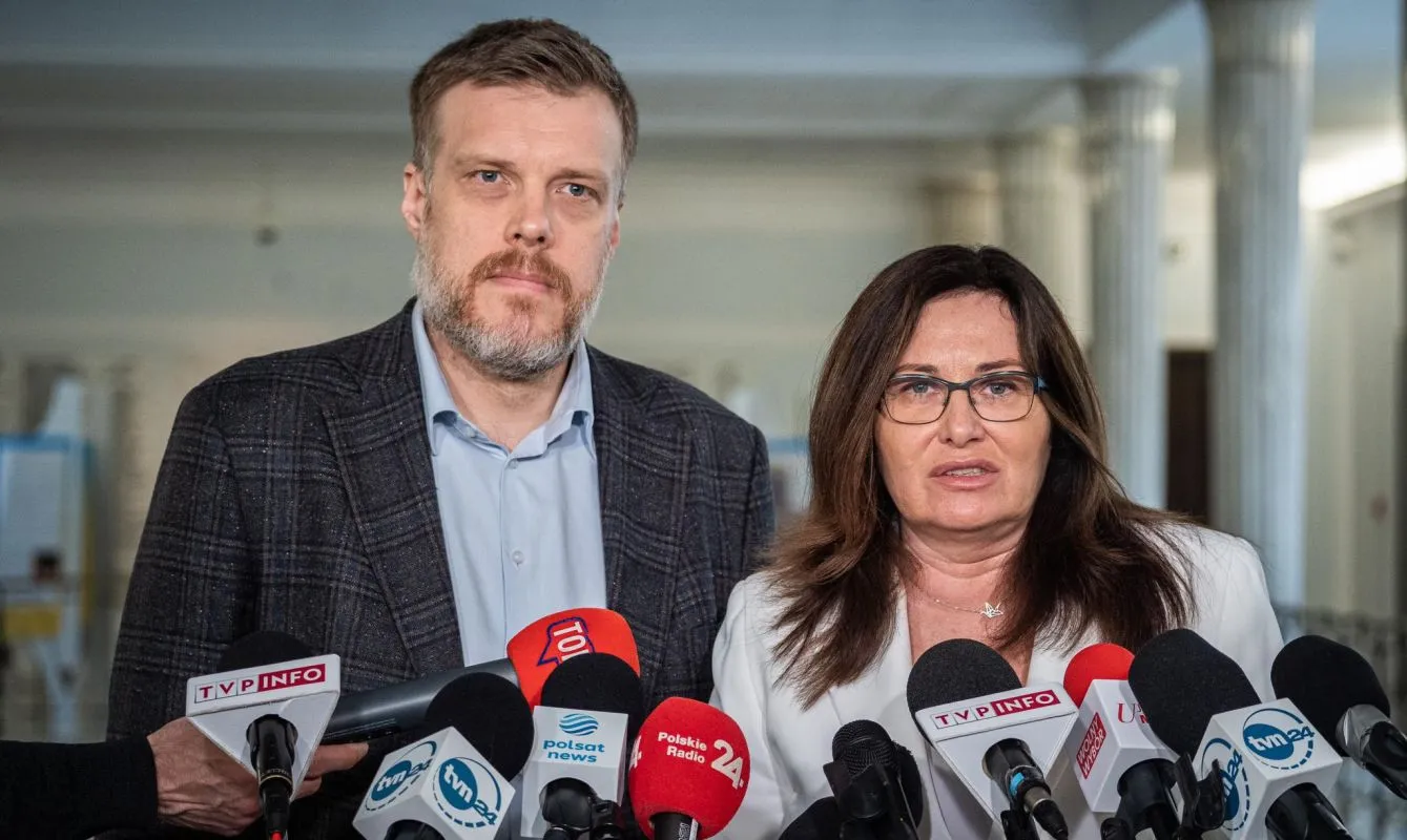 Dwoje osób podczas konferencji prasowej o WIBOR w wnętrzu budynku, kobieta z okularami po prawej, mężczyzna po lewej, otoczeni mikrofonami dziennikarzy.