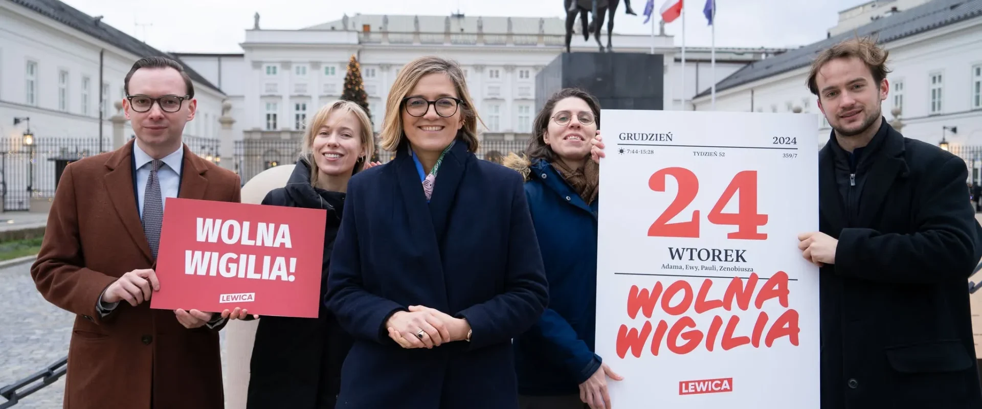 Grupa pięciu osób stoi na placu, trzyma plakaty z napisem 'WOLNA WIGILIA' na tle konnego monumentu i budynków.