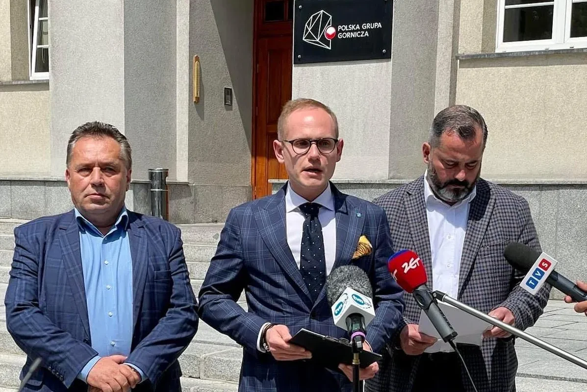 Na zdjęciu trzech mężczyzn stoi przed budynkiem, gdzie odbywa się konferencja prasowa, trzymając mikrofony i dokumenty.