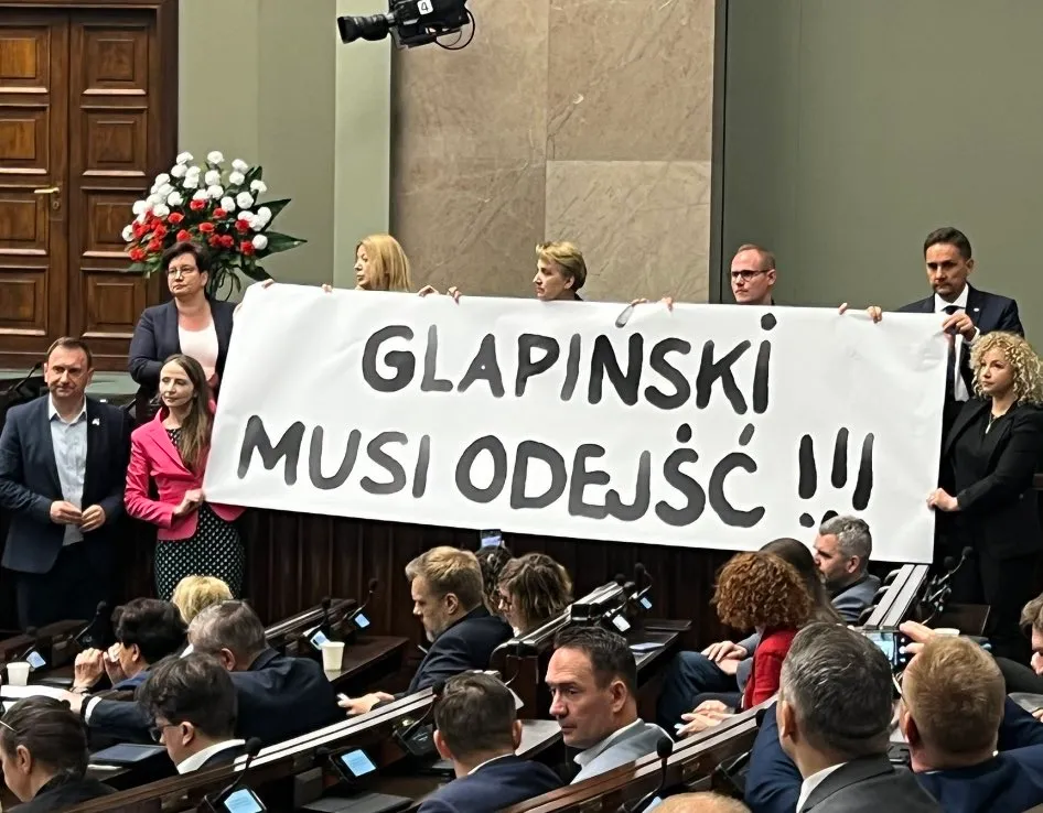 Na zdjęciu członkowie parlamentu trzymają transparent z hasłem "GLAPIŃSKI MUSI ODEJŚĆ" podczas posiedzenia.