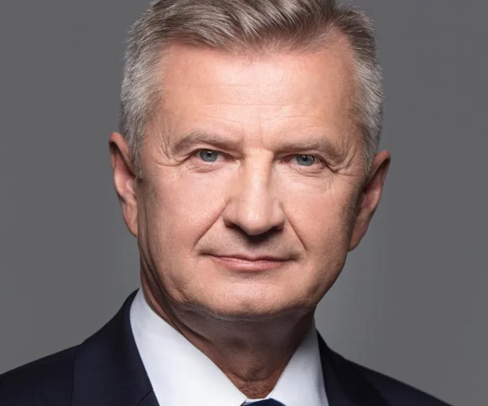 Portret mężczyzny w garniturze na szarym tle, w kontekście rozmów o dronach dla polskiej armii.