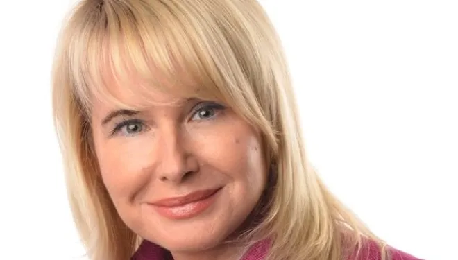 Portret uśmiechniętej kobiety o blond włosach i delikatnym makijażu na białym tle.
