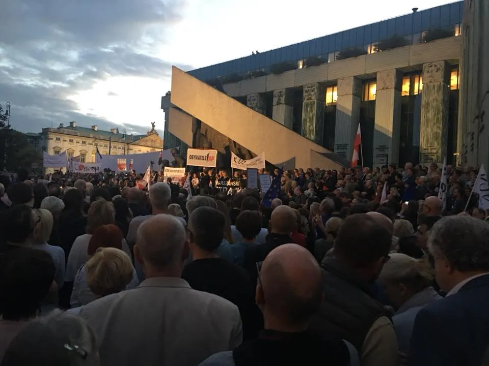Duży tłum uczestników demonstracji trzyma banery i flagi przed nowoczesnym budynkiem podczas protestu w obronie wolnych sądów.
