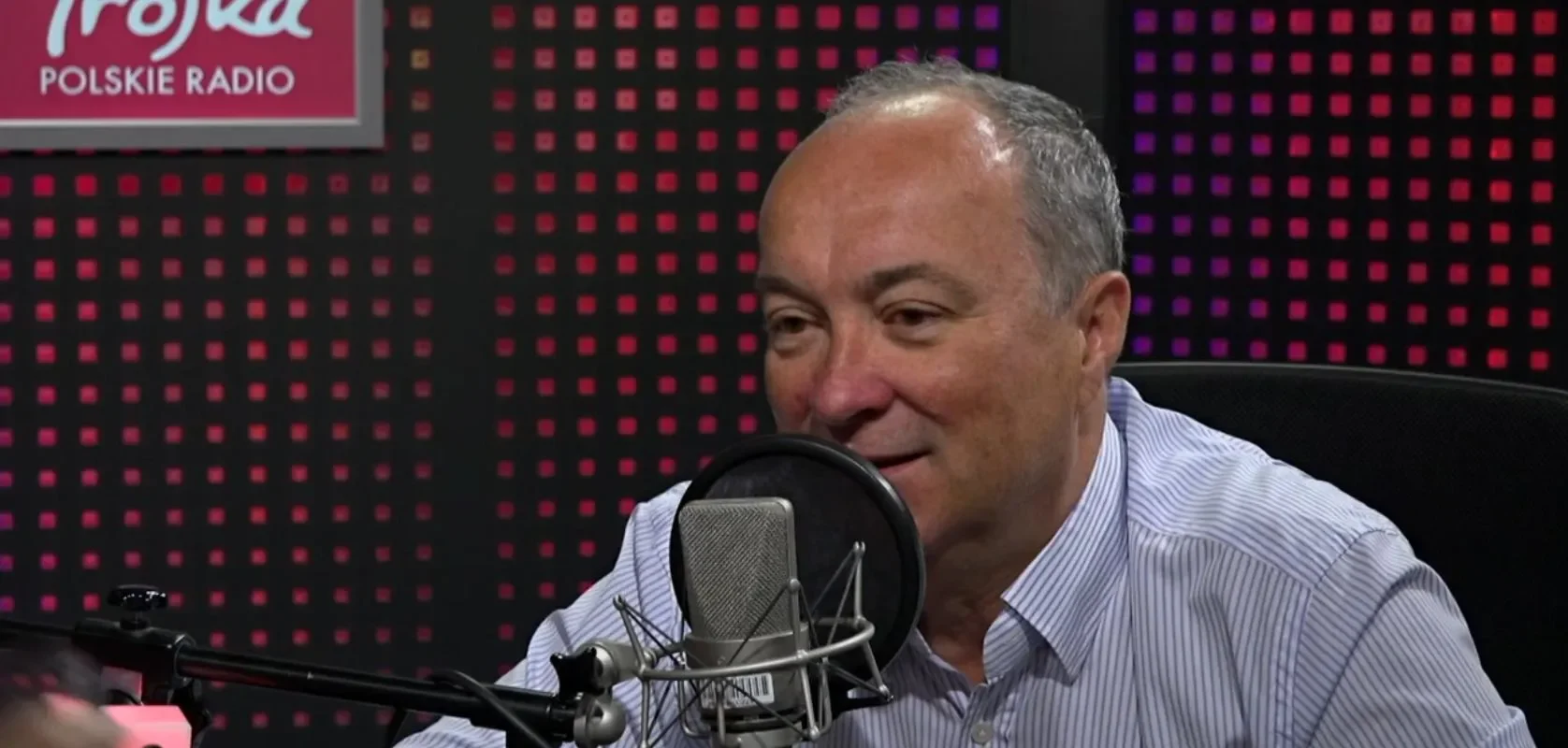 Mężczyzna w koszuli siedzi przy mikrofonie w studiu radiowym Trójka Polskie Radio.