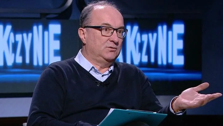 Osoba w okularach siedzi w studiu telewizyjnym, gestykuluje jedną dłonią i trzyma dokumenty podczas rozmowy o likwidacji IPN.