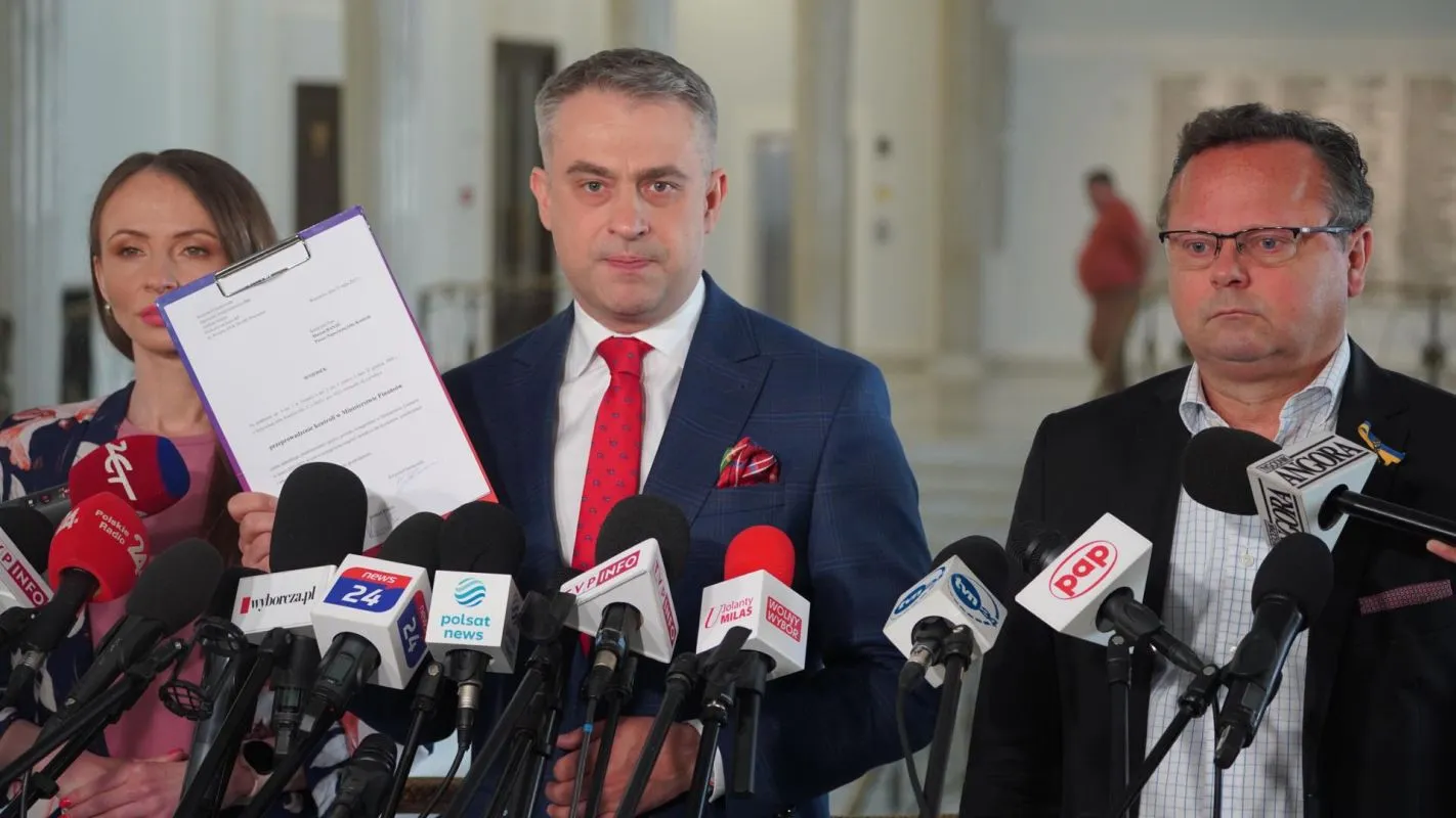 Grupa polityków Lewicy na konferencji prasowej domagającej się kontroli bonusów Polskiego Ładu; jeden z nich trzyma dokumenty przed licznymi mikrofonami.