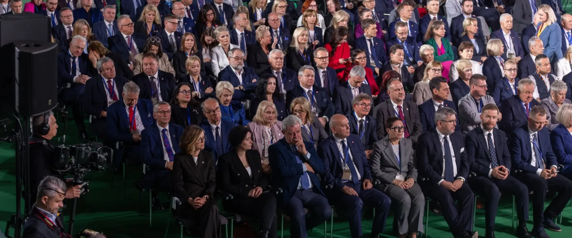 Szeroka sala pełna uczestników w formalnych strojach siedzi w rzędach podczas wydarzenia upamiętniającego 1000. rocznicę koronacji Bolesława Chrobrego.