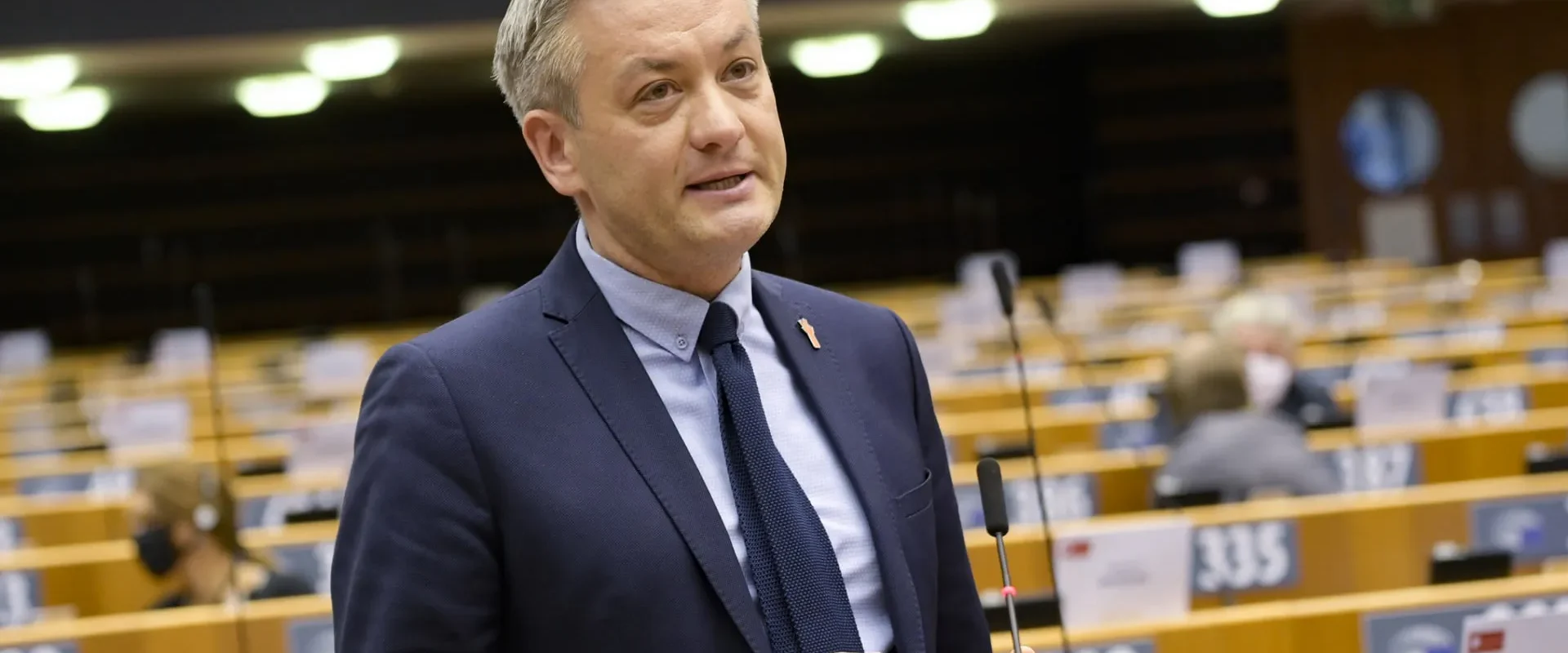 Mężczyzna w garniturze przemawia do mikrofonu w sali plenarnej, w tle ustawione miejsca dla posłów, w kontekście prac nad Europejską Kartą Praw Kobiet.