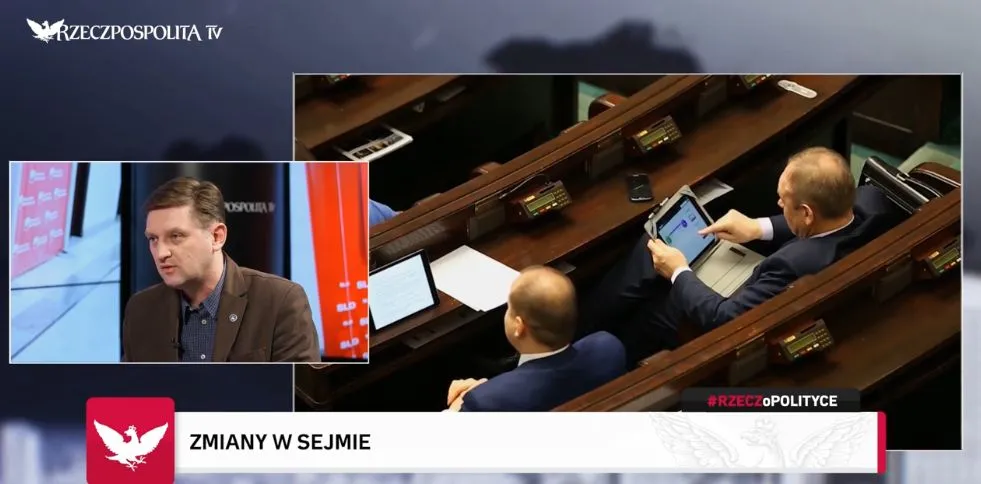 Zrzut ekranu programu informacyjnego z podzielonym obrazem: w małym okienku rozmówca, a w głównym ujęciu z sali Sejmu kilku posłów siedzi na ławach, jeden mężczyzna korzysta z tabletu.