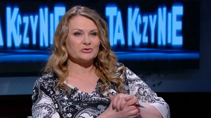 Kobieta z blond włosami w wzorzystej bluzce rozmawia w studiu telewizyjnym, a w tle widoczne są niebieskie napisy.