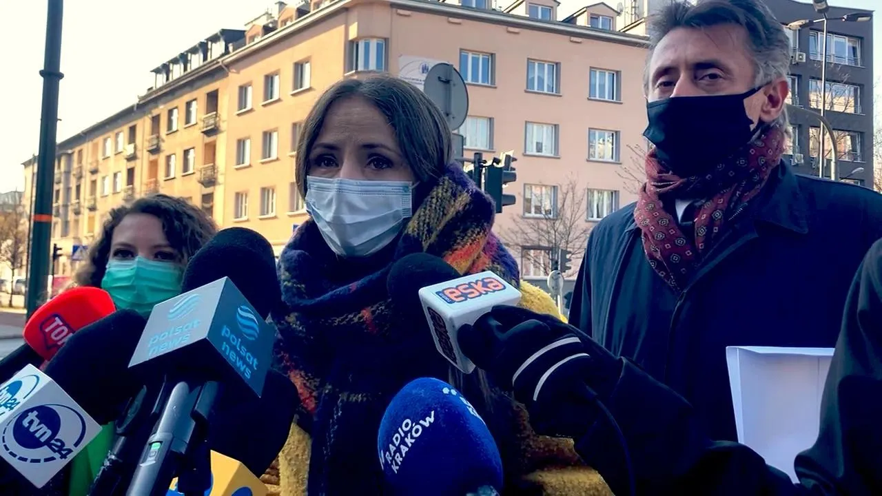 Trzy osoby w maseczkach stojące przed zestawem mikrofonów dziennikarzy podczas konferencji prasowej na zewnątrz budynku Małopolskiego Kuratorium Oświaty podczas kontroli poselskiej.