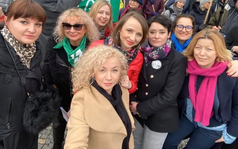 Grupa kobiet uczestniczących w Manifie „Feminizm dla klimatu, klimat na antykapitalizm” uśmiecha się do kamery, stojąc w tłumie.