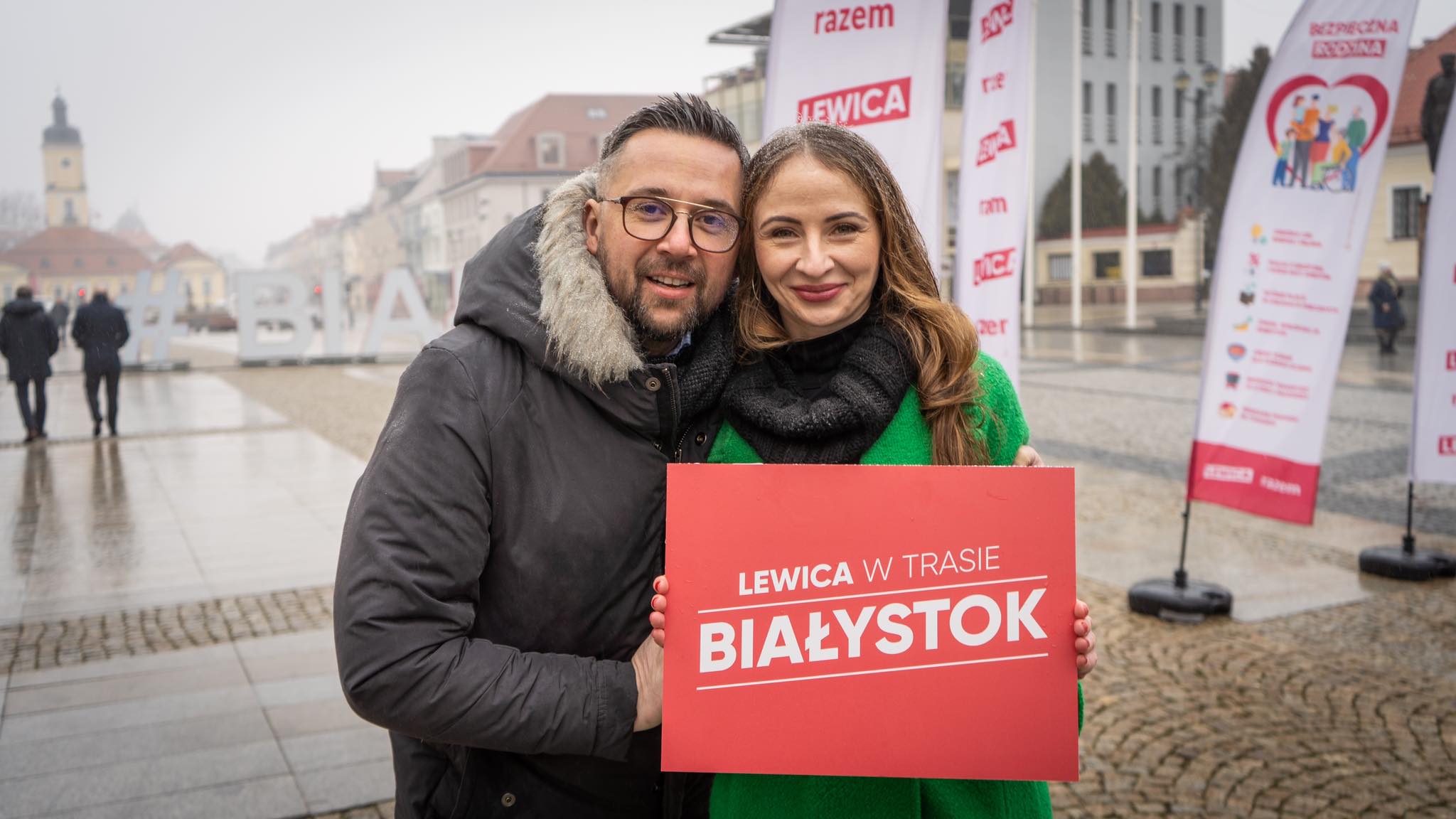 Na zdjęciu widoczni są uśmiechnięci mężczyzna i kobieta trzymający czerwony znak z napisem 